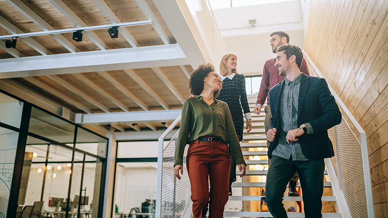 Four employees walking down the interior hallway stairs of their office building