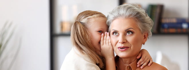 Granddaughter whispering into grandma`s ear