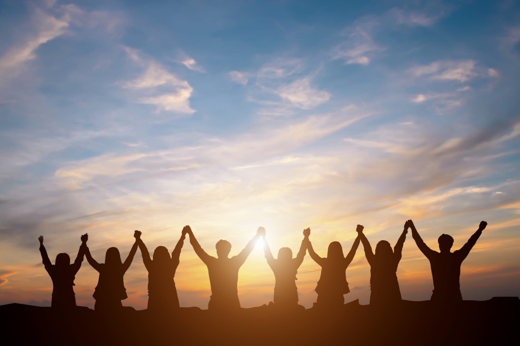 A line of people raise their hands into the air victoriously against a sunset sky