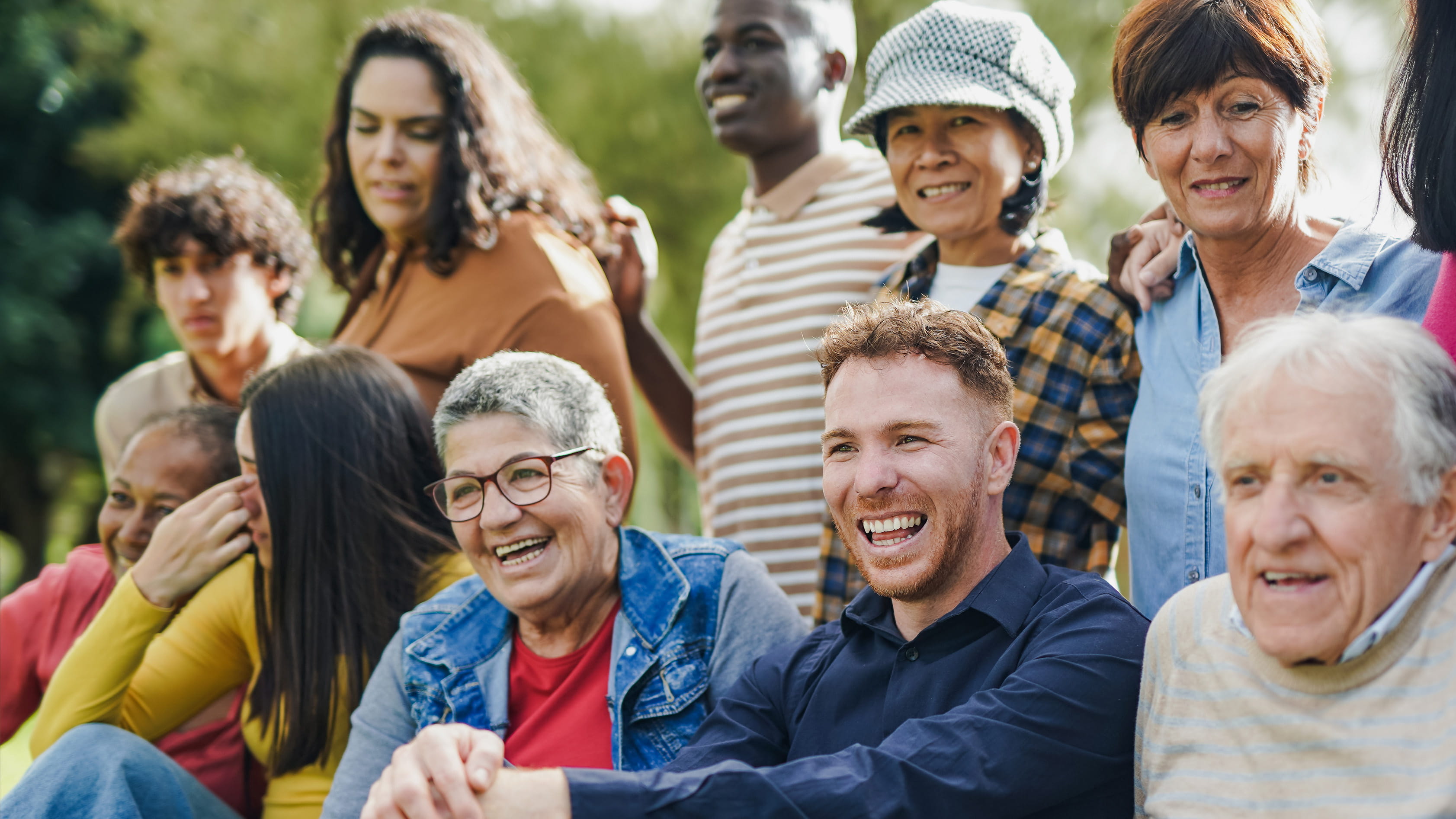 Multigenerational, multiracial group poses for photo in two rows while laughing