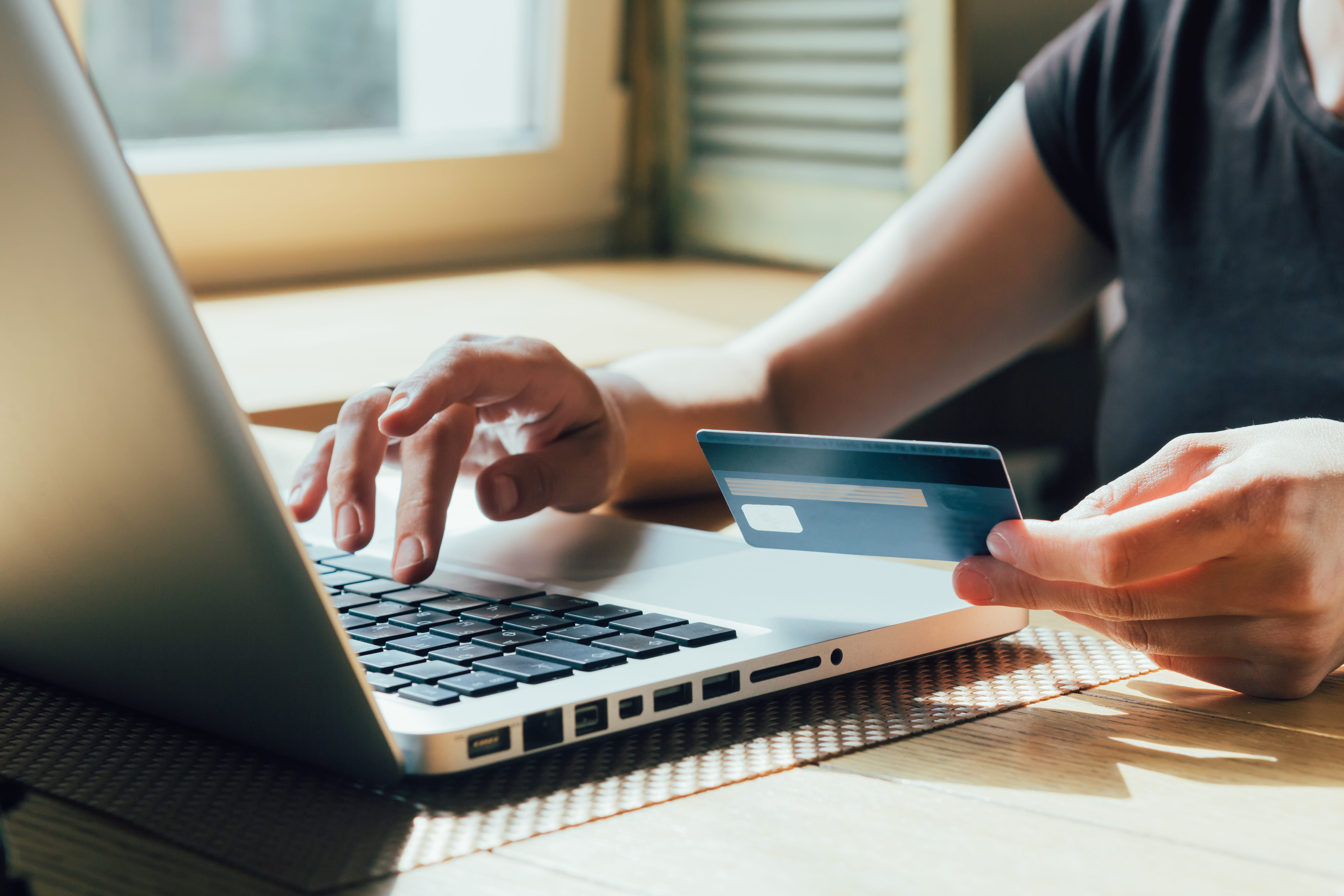 Credit card being held by woman typing on the laptop computer.