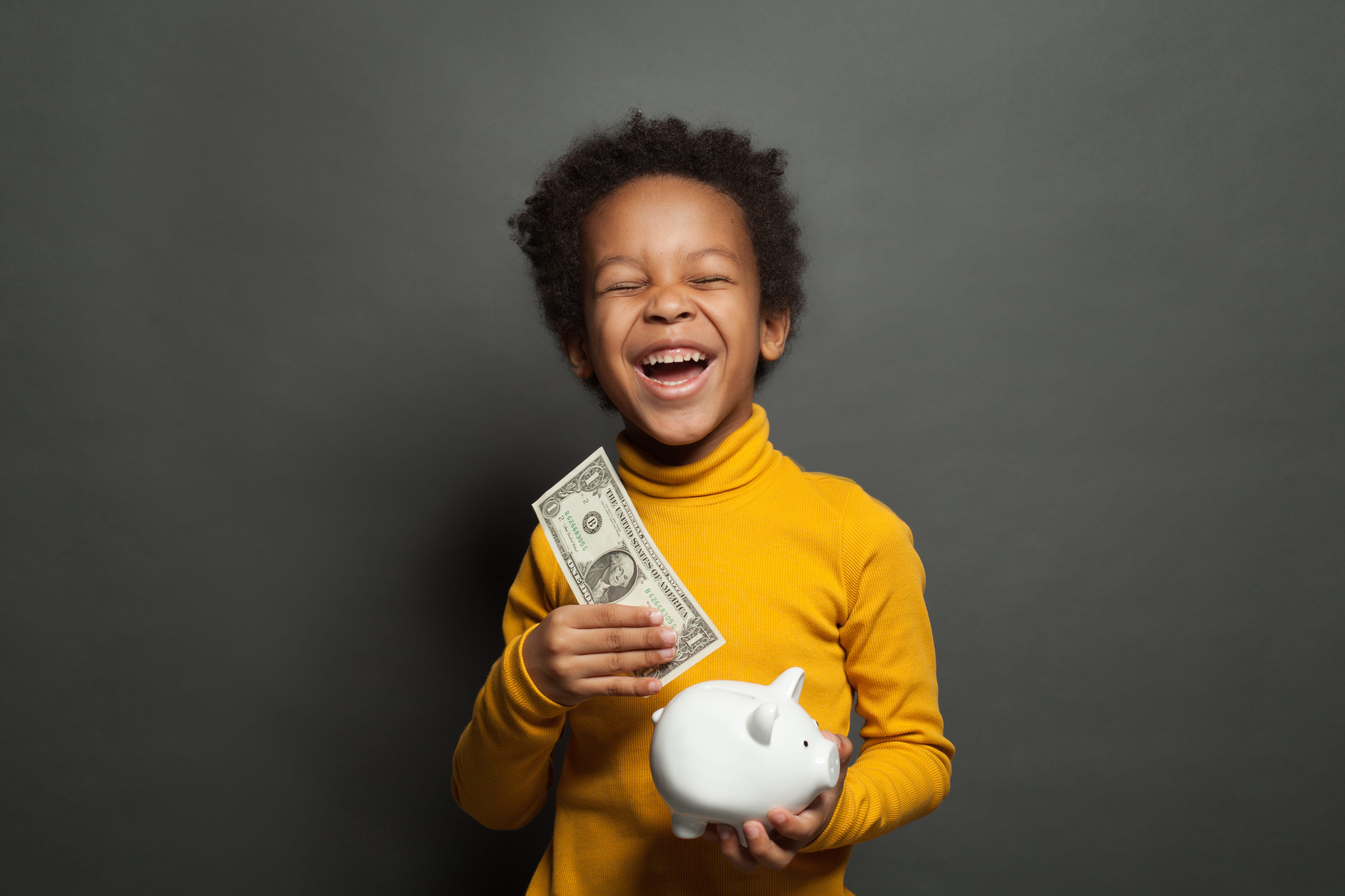 Child with yellow turtleneck puts a dollar into a piggy bank.