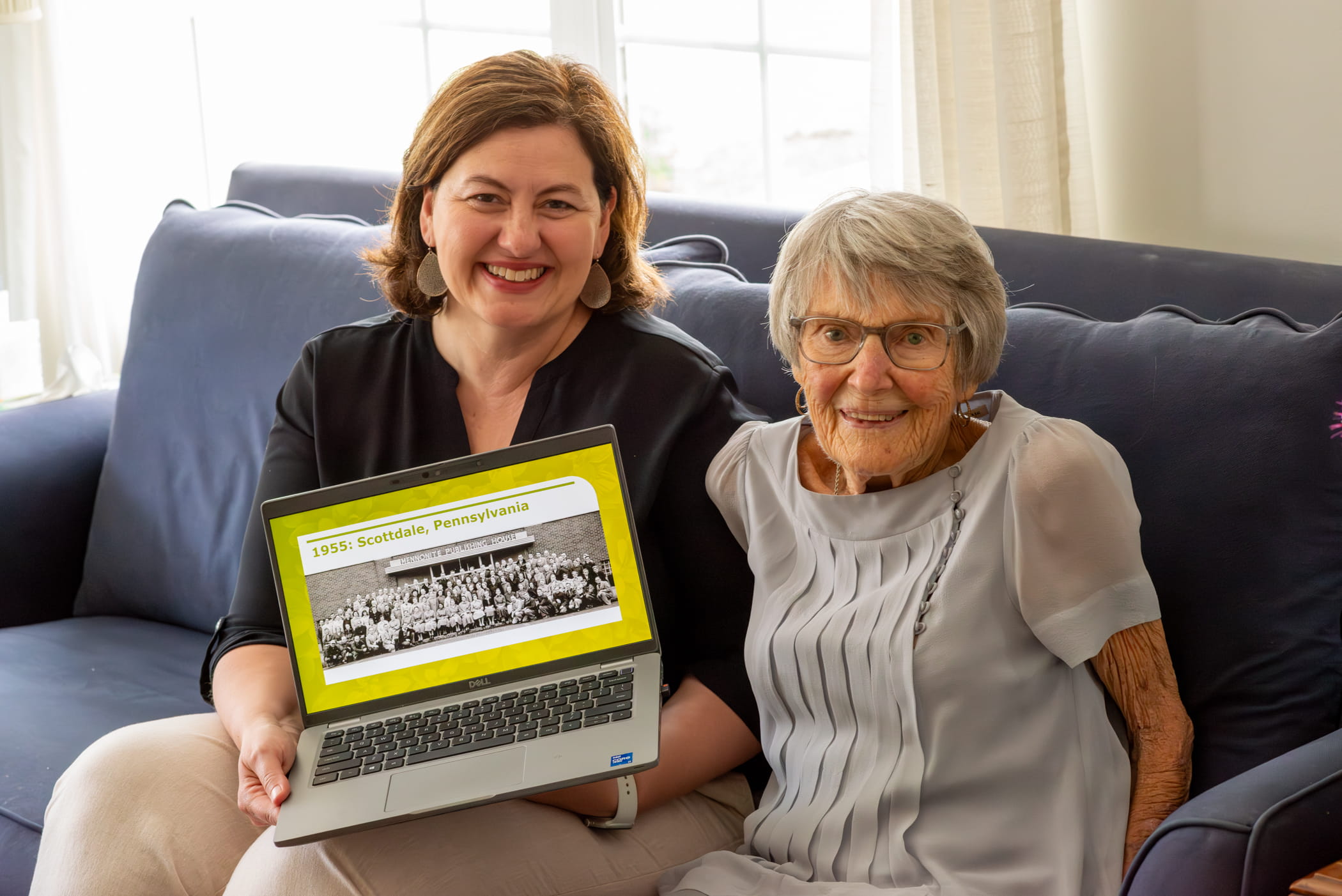 Arlene Miller, member number one of the credit union, and Kristen Heisey, EFCU president, smile with a laptop showing the original founders of the credit union.