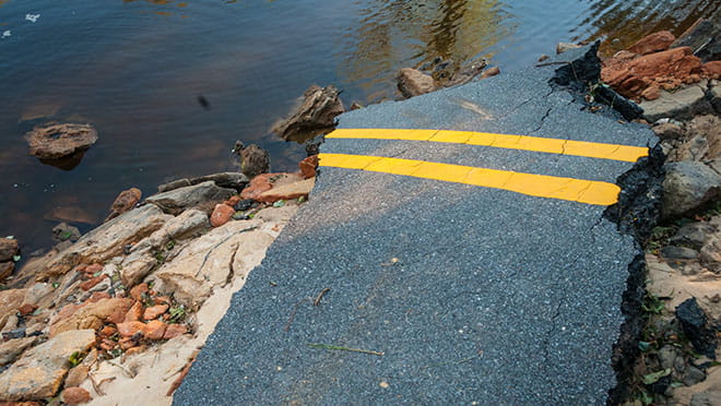 A piece of hurricane-damaged pavement sits atop rocks on a flooded road.