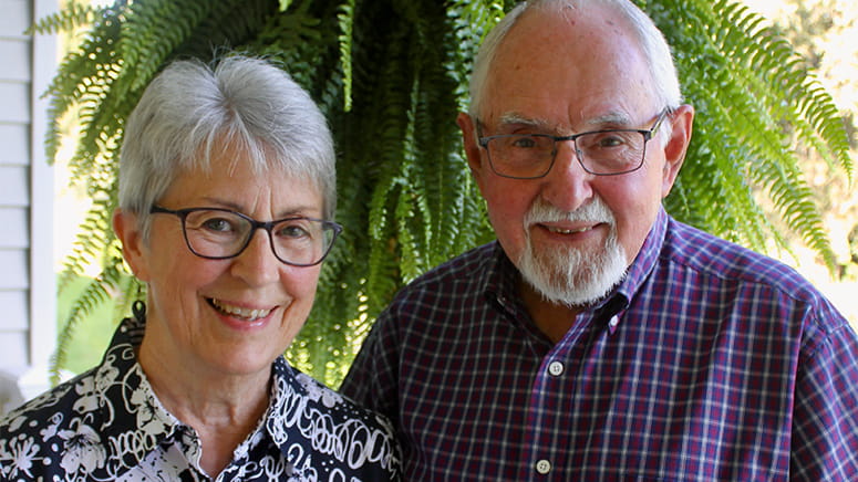 Mary and Ervie Glick, standing with green hanging fern in background