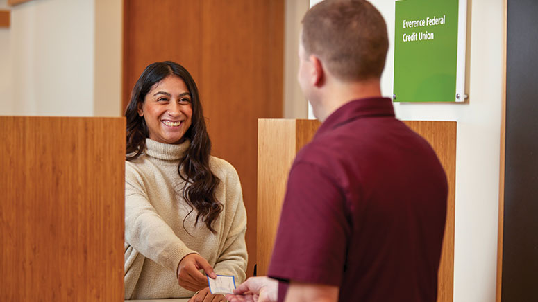 A man and women looking at each other, smiling; both are holding a check like one is handing it to the other