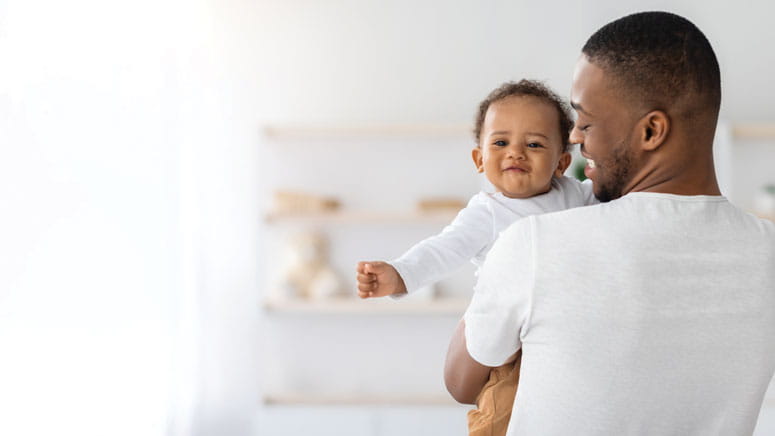 A man holding a baby. He is smiling at the baby, while the baby smiles at the camera