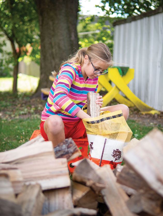 A girl places cut firewood into a sack