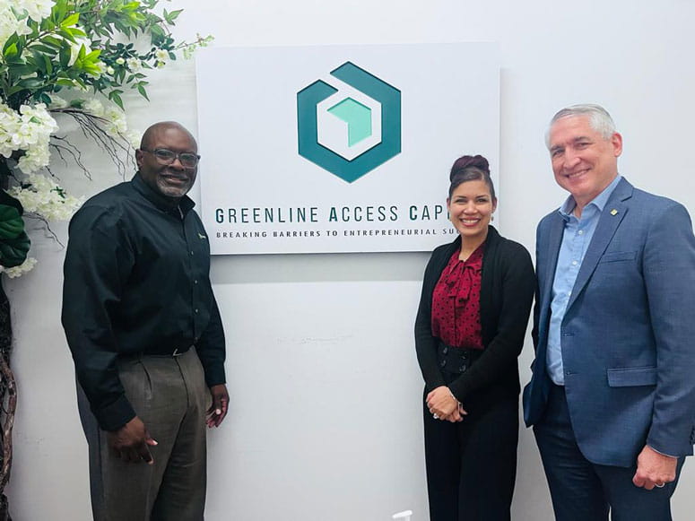 Leonard Dow, Ken Hostetler and a woman stand, posing, in front of a sign that reads "Greenline Access Capital."