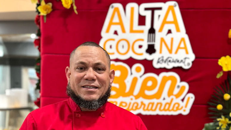 A photo of a man, from the upper chest up, with a sign in the background. the sign reads "Alta Cocina Restaurant"