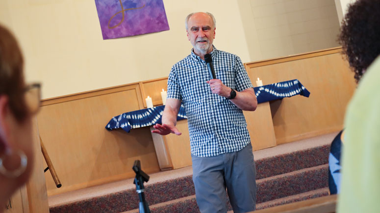 A man standing at the altar in a church hold a microphone and speaks to a crowd