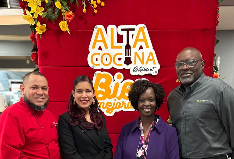 Two men and two women stand, posing for a photo. A sign in the background reads "Alta Cocina Restaurant."