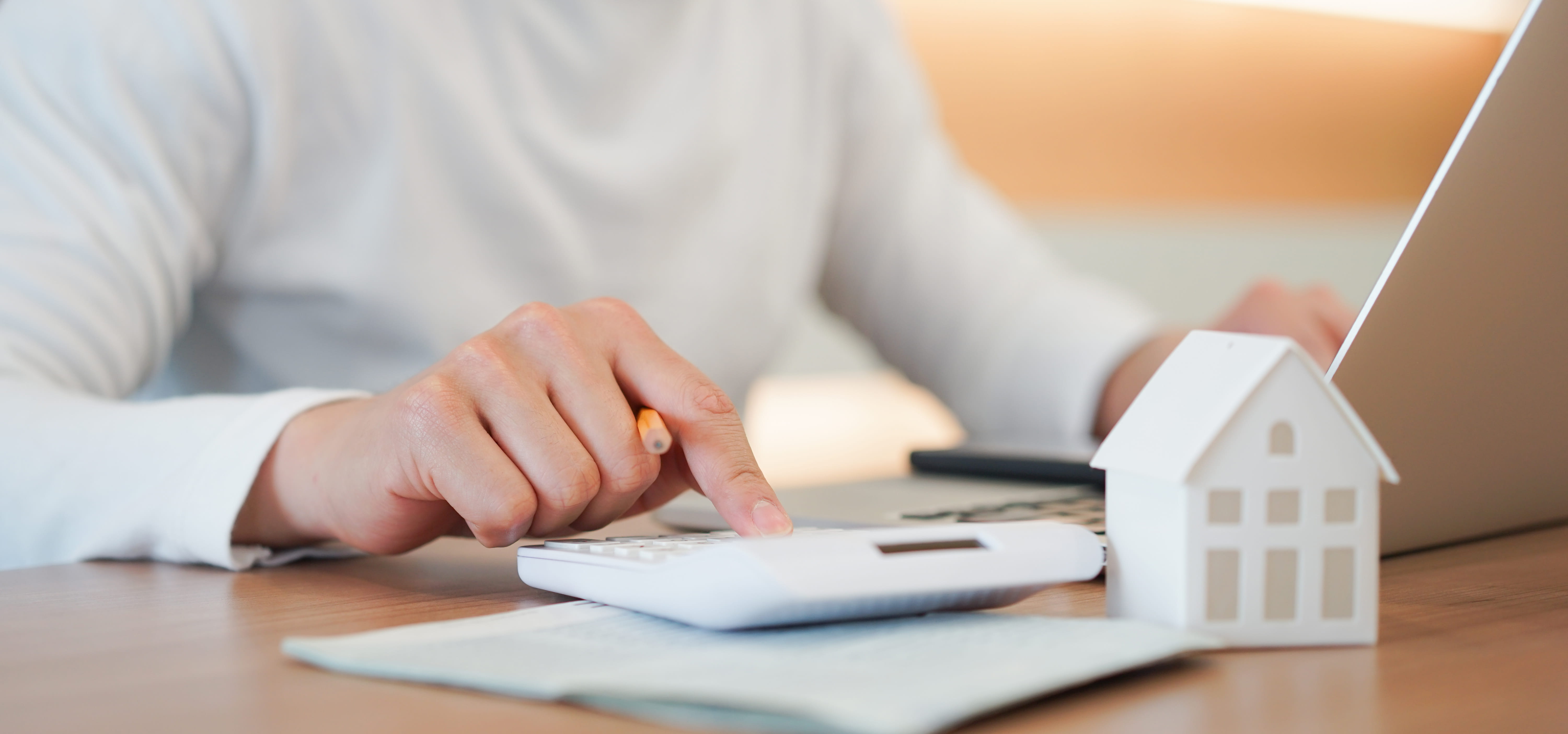 Man working on a calculator and laptop with a small house statue on the desk.