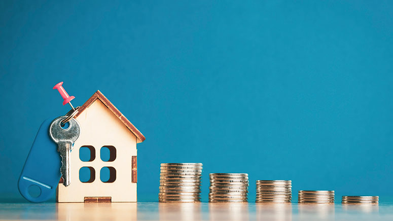 Piles of coins with wooden house with house keys pinned to it