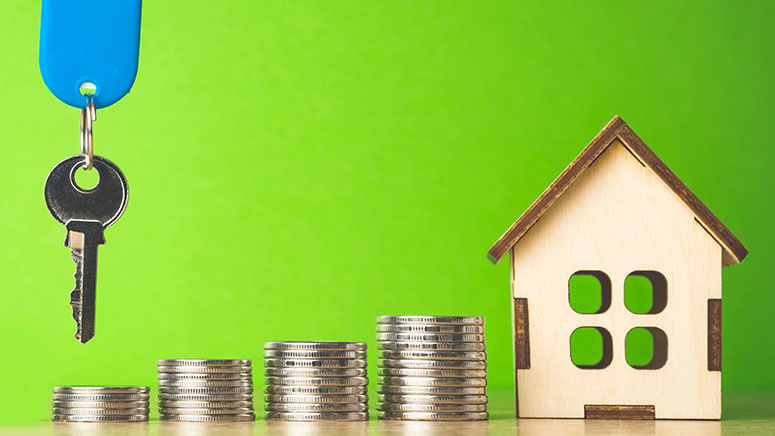 Piles of coins with dangling house key and wooden house