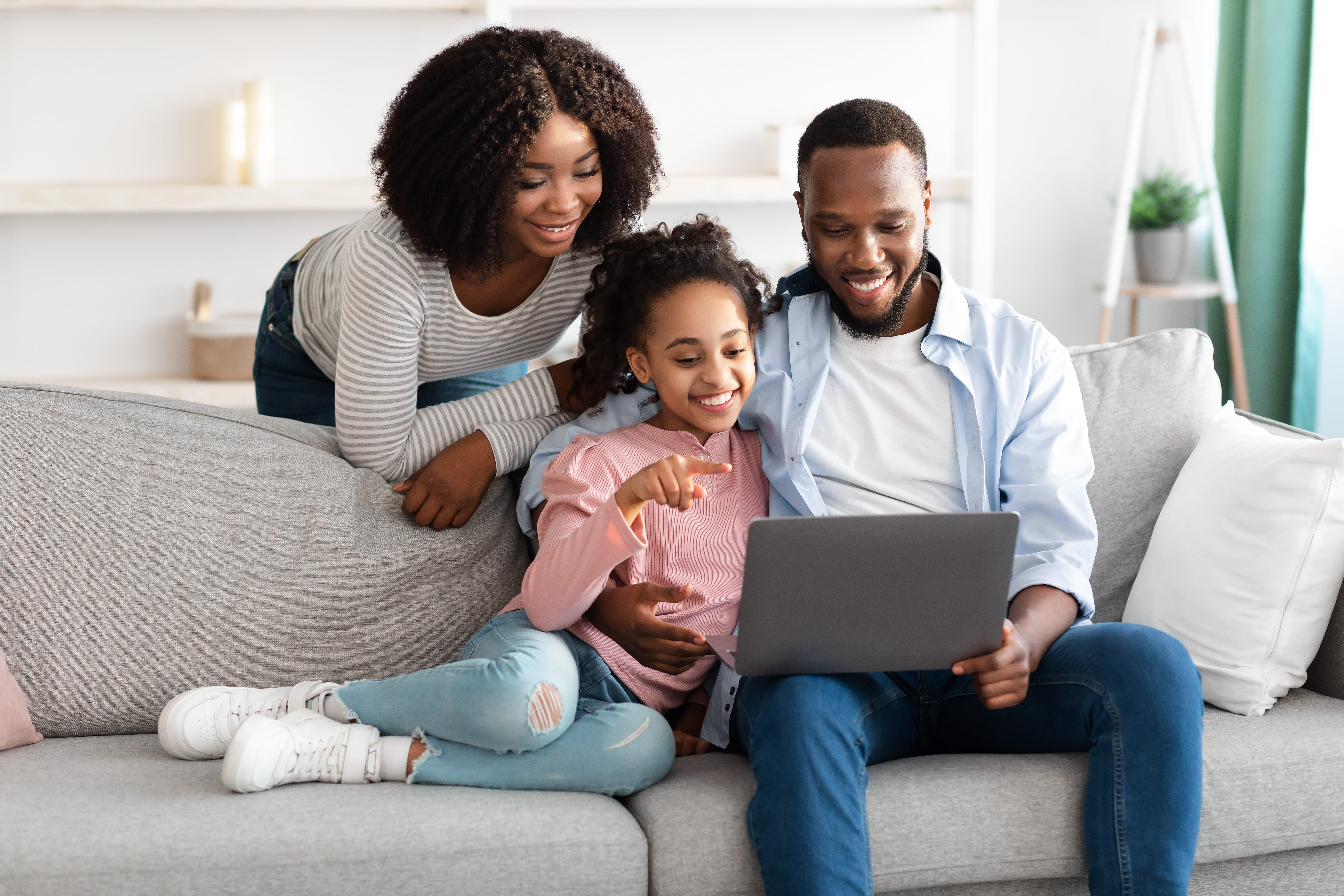 Black family of three sits on the couch happily looking at a computer together.