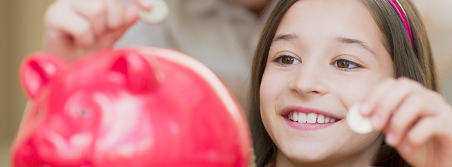 Young girl dropping coins into a piggy bank