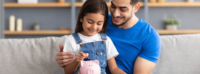 Little girl putting money in piggy bank