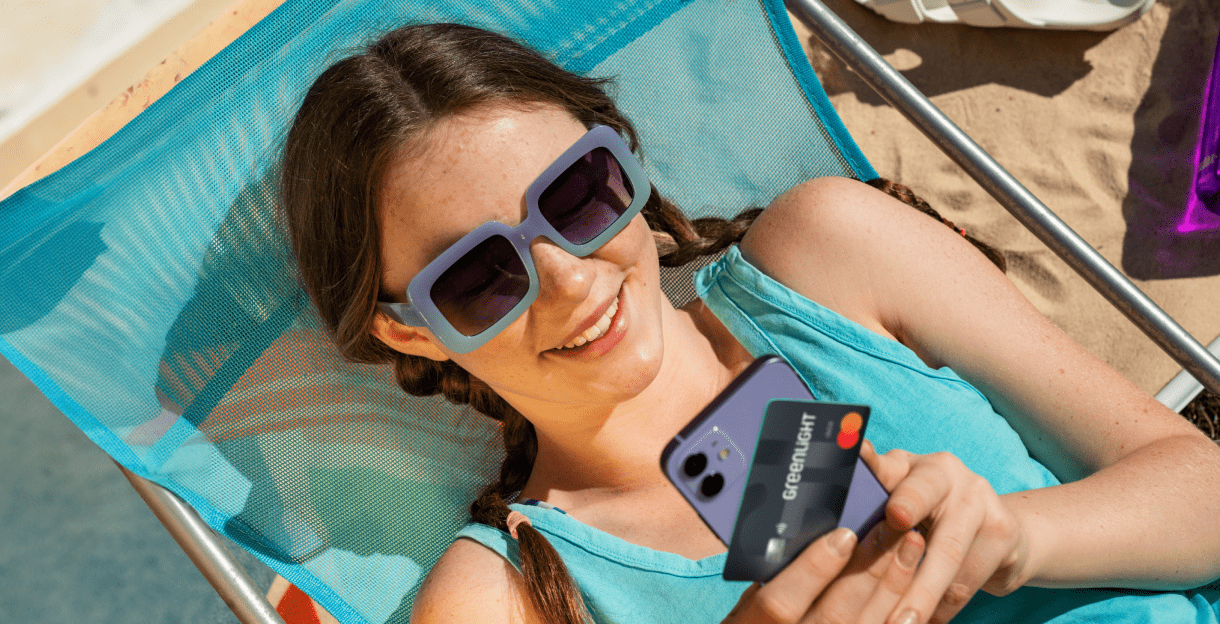 Girl at the beach looking at her phone and debit card.