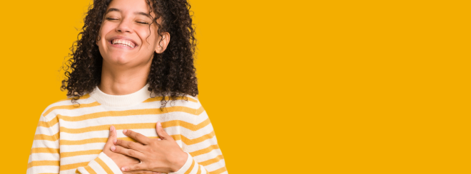 Young woman holding hands over heart on bright orange background