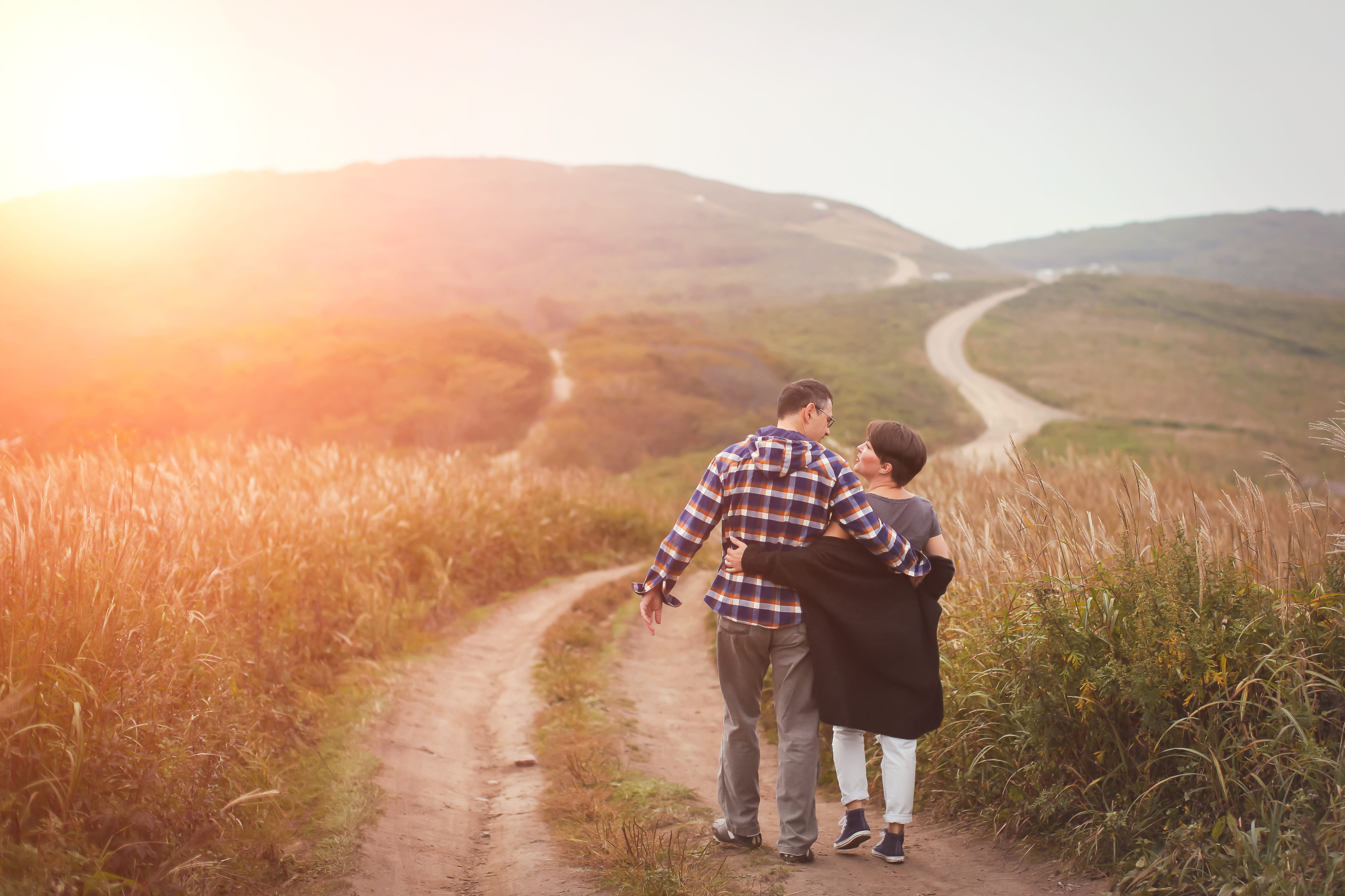 Couple walks on a dirt path through a field in sunrise