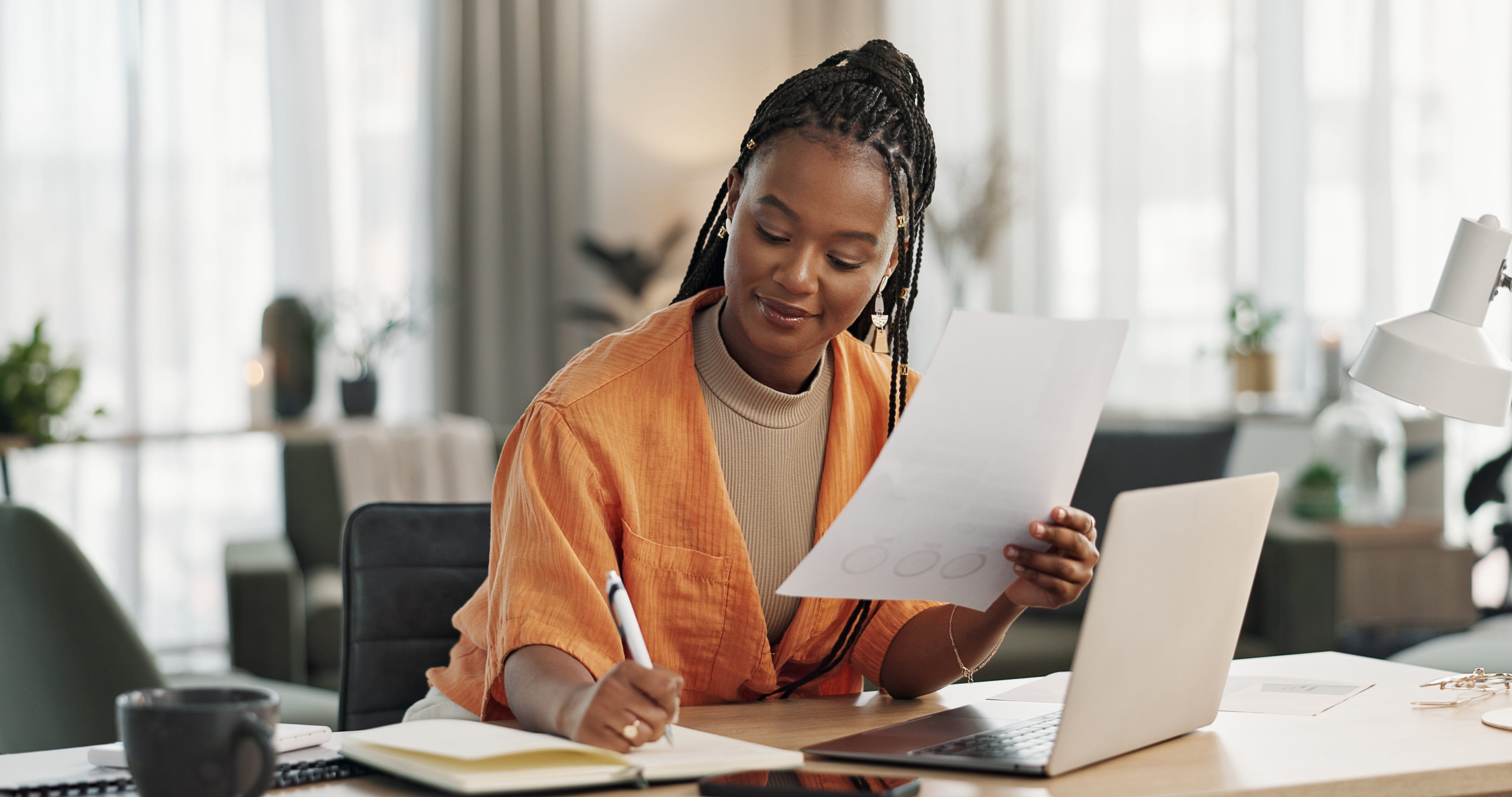 Woman working at laptop with pen and paper