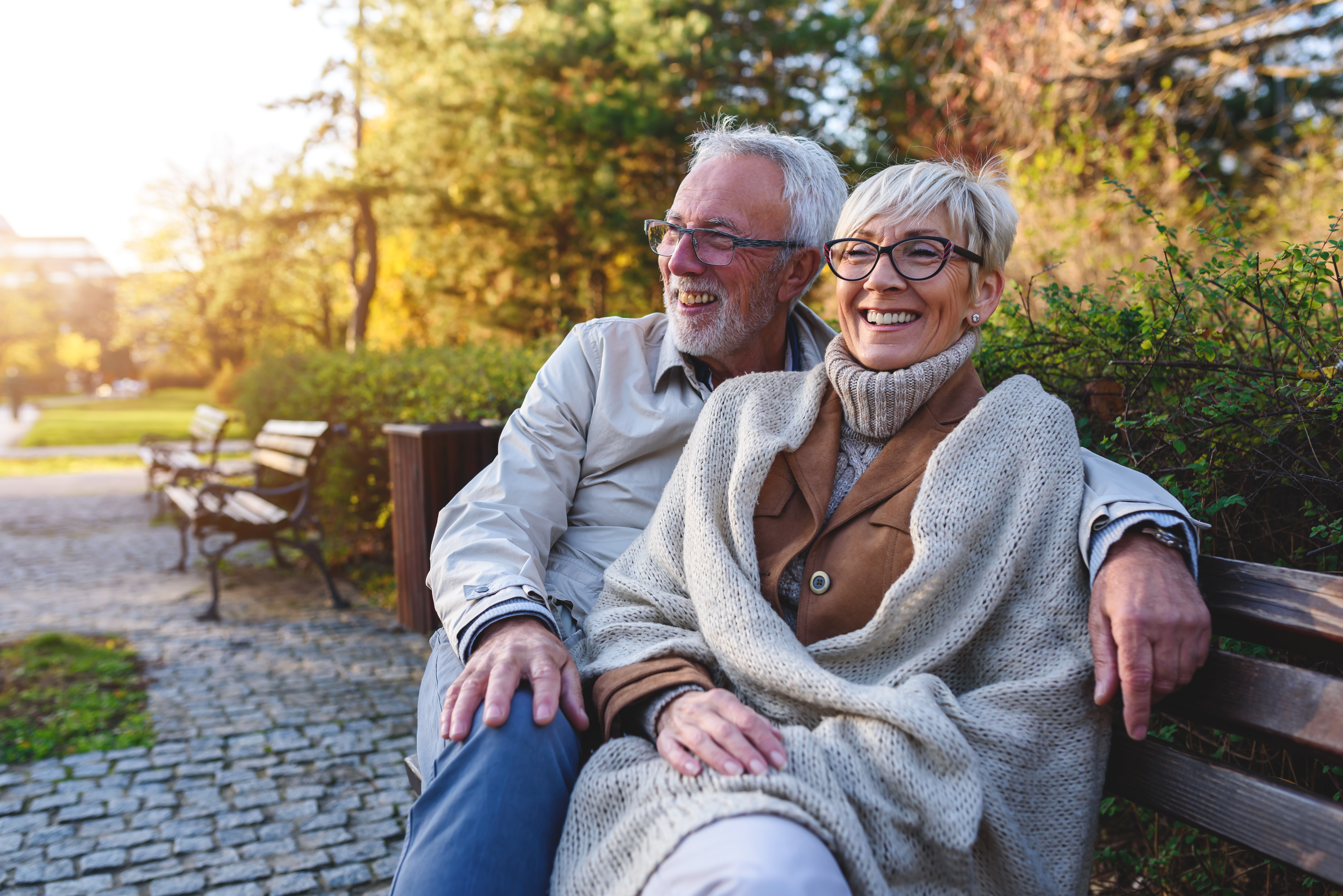 Older couple smiling and laughing sitting on a park bench at golden hour.