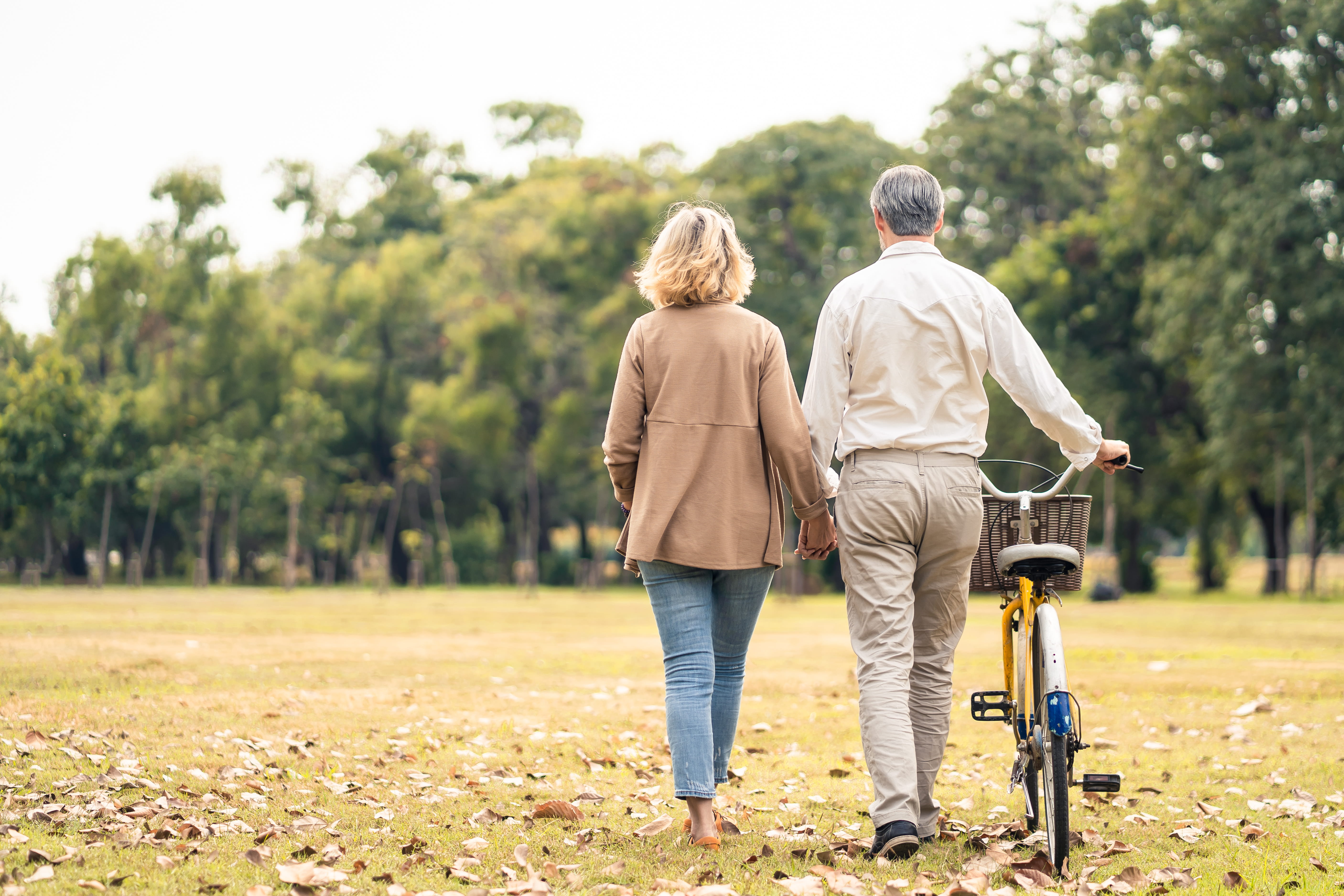 A middle-aged couple walks a bike through a field.