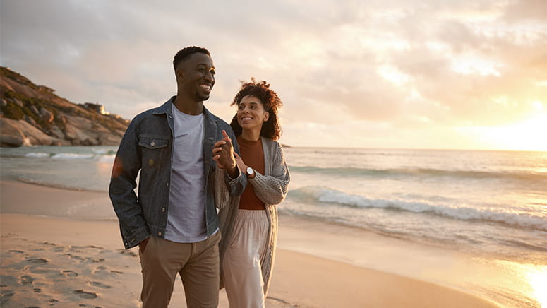 Black couple smiling and walking on beach at sunset