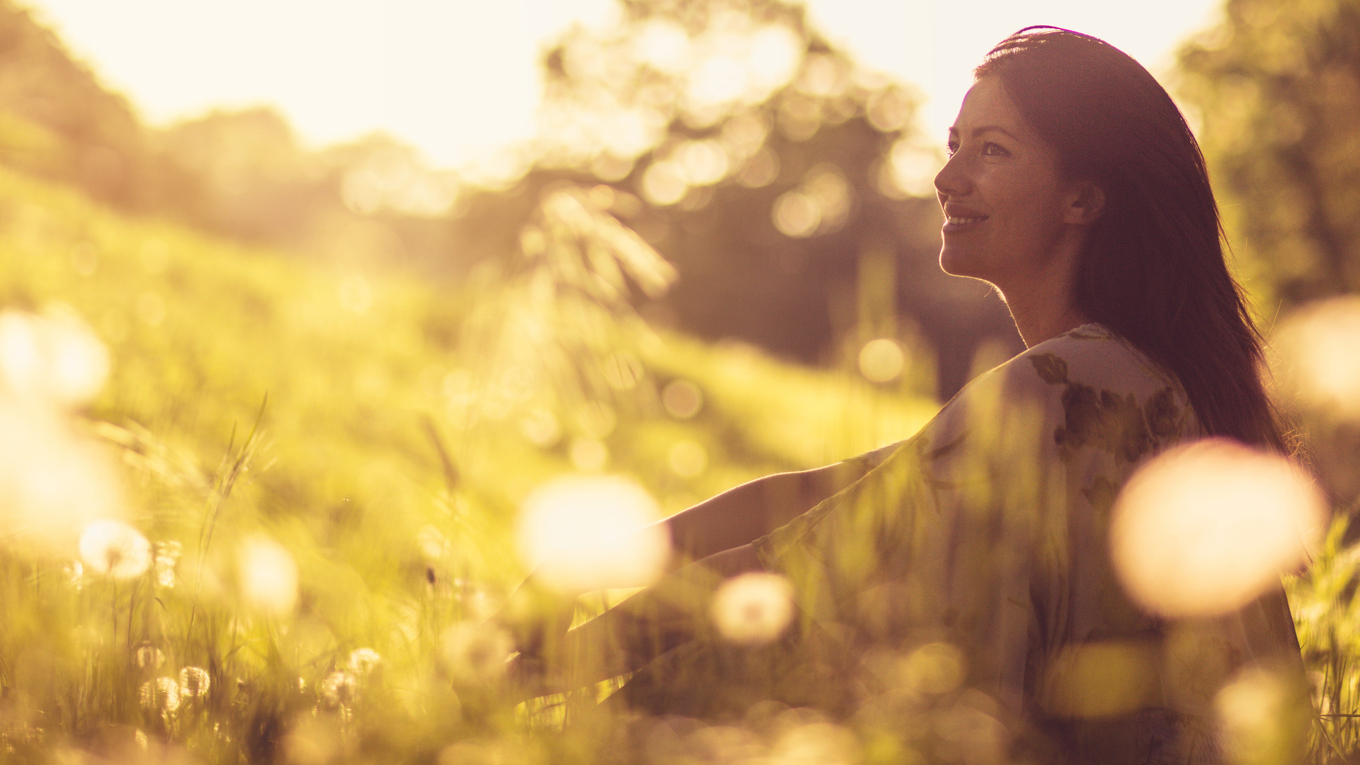 Woman sitting on a hill in silhouette with sun.