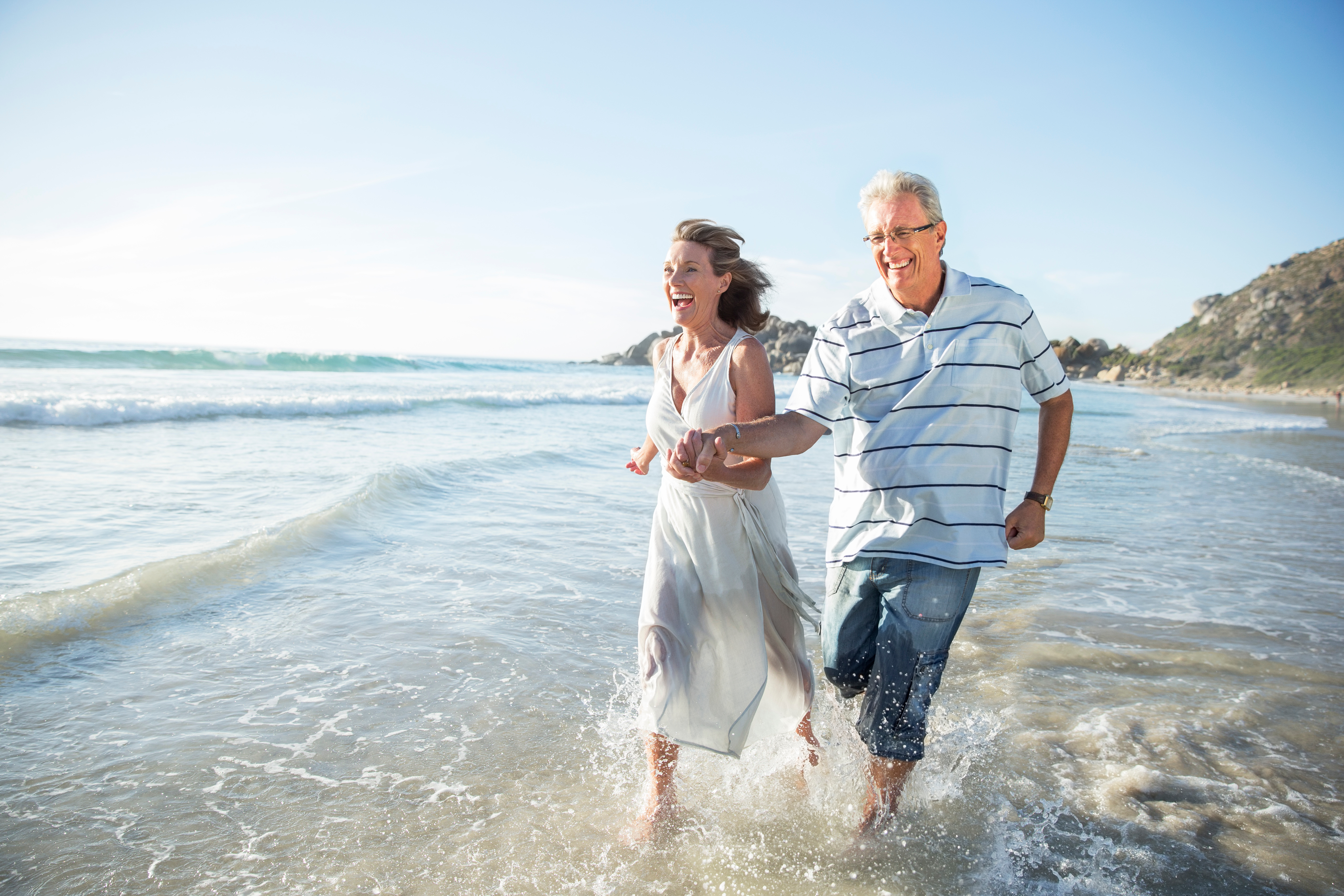 Older couple runs into the water at the beach while smiling.