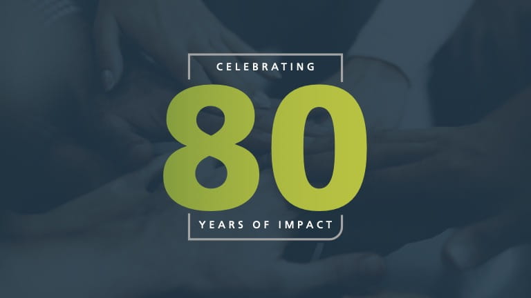 Hands piled in under a blue overlay covered by the text "Celebrating 80 years of impact"