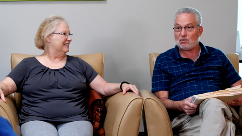 A senior couple sitting in oversized chairs discussing.