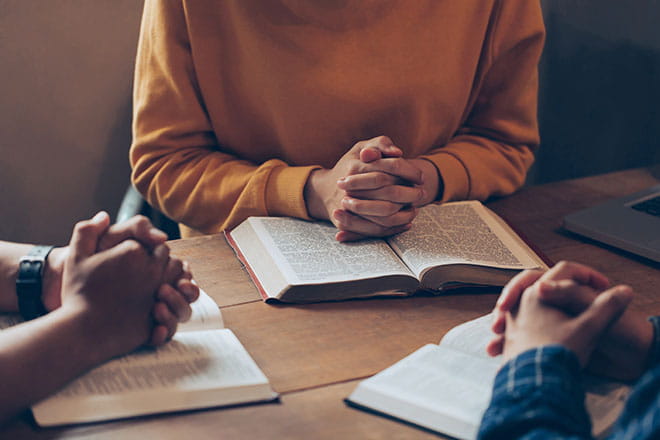 Three people praying over open bibles