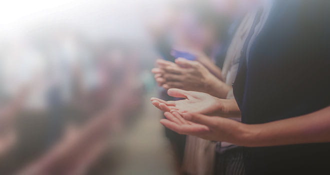 People in church pews worshiping with open hands